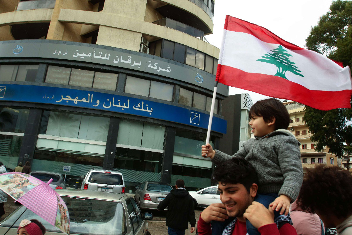 A Lebanese protester carries a child as he takes part in a rally in front of a bank in the southern city of Sidon (Saida) on December 30, 2019