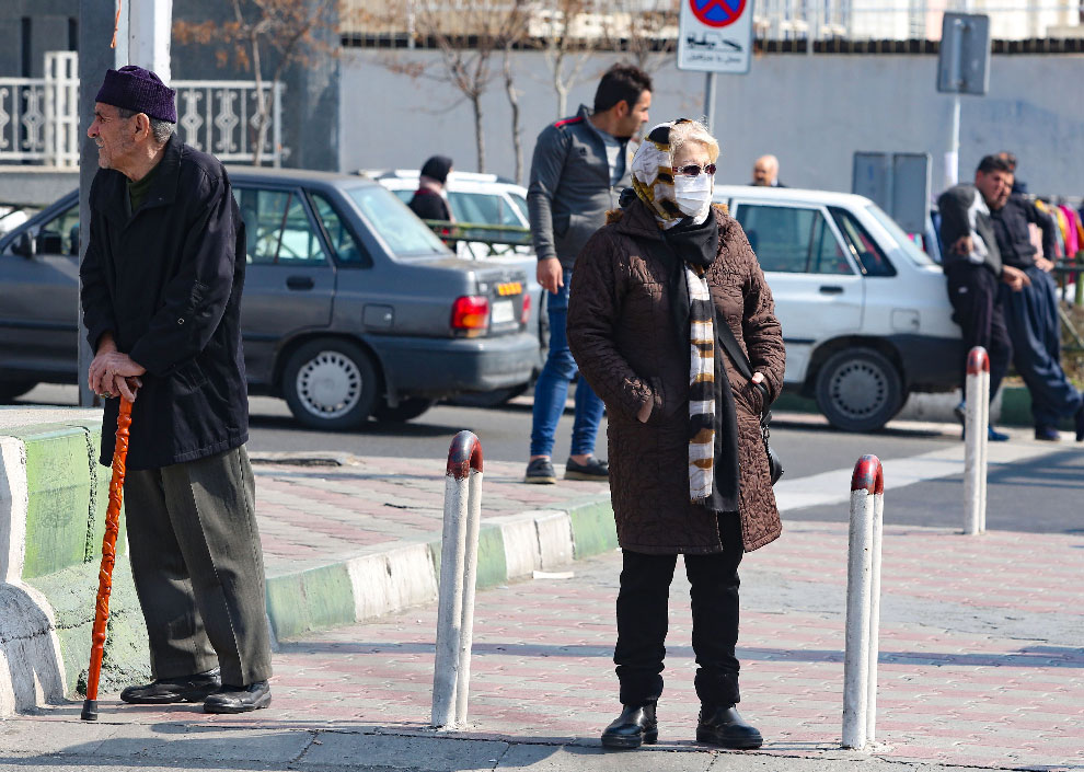 An Iranian woman wearing a protective mask and gloves, stands in a busy street in the capital Tehran