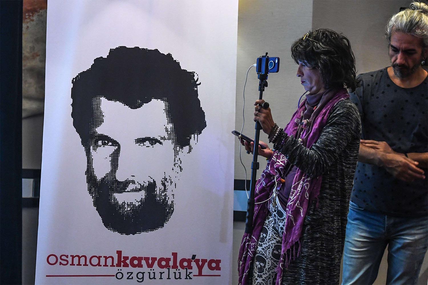 A journalist stands in front of a poster featuring businessman and philanthropist Osman Kavala