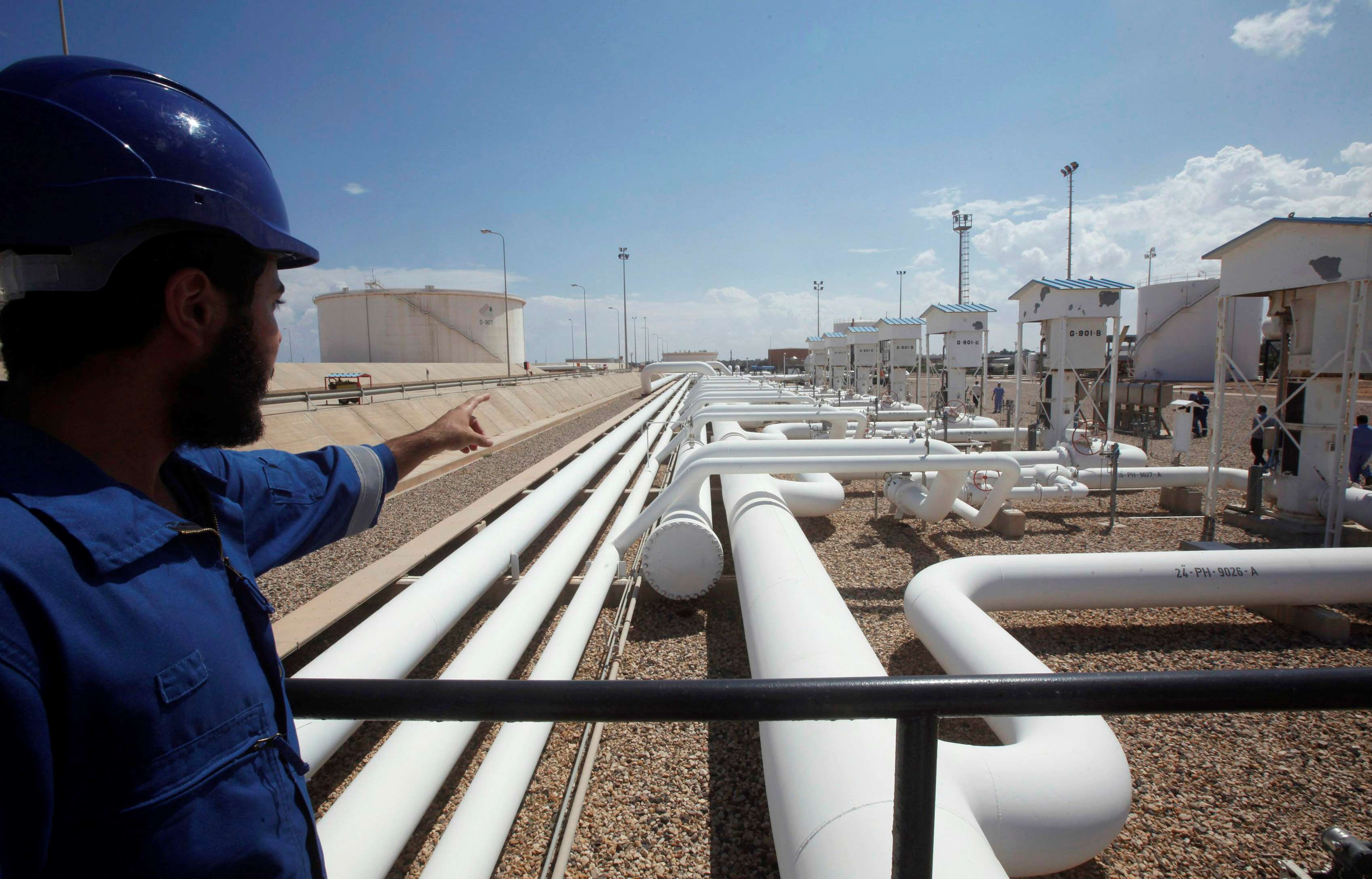 A worker gestures towards pipelines at the port and Zawiya Oil Refinery