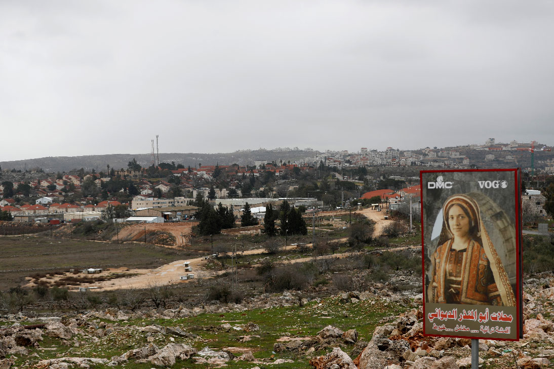 A sign for a Palestinian clothing shop is seen in the village of Silwad as the Jewish settlement of Ofra appears in the background