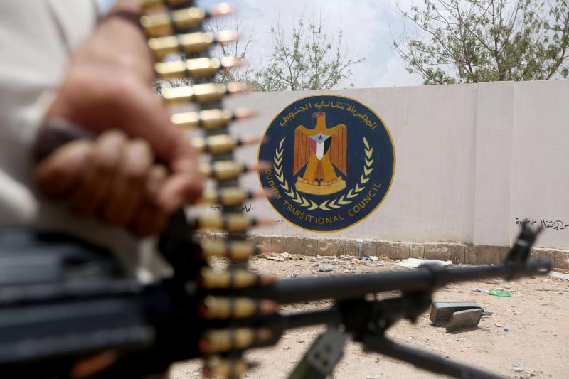 A Yemeni government soldier holds a weapon as he stands by an emblem of the Southern Transitional Council