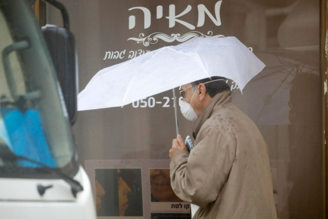 A man walks with umbrella and a mask in Hadera