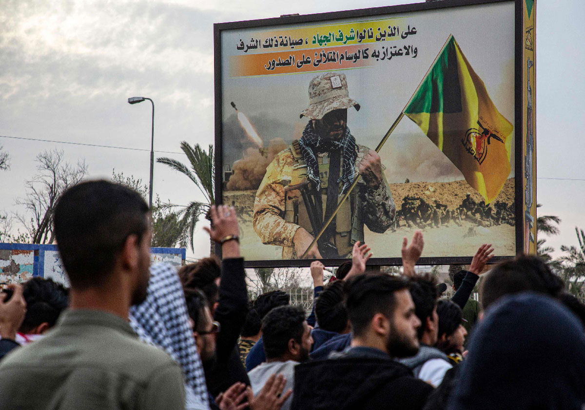 Protesters chant slogans as they walk past a Kata'ib Hezbollah's billboard during an anti-government demonstration in Basra