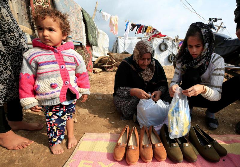 Syrian refugees hold bags of gloves for preventing the coronavirus' spread, in al-Wazzani area in southern Lebanon