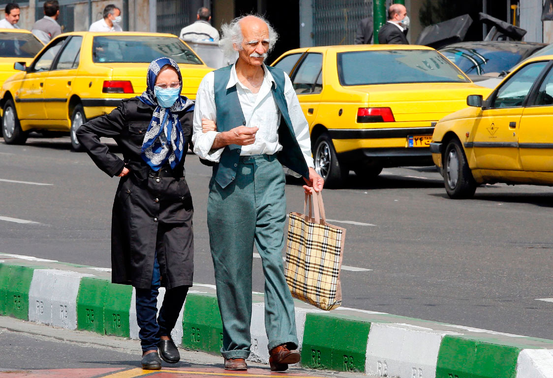 An elderly man and a woman, wearing a protective mask, walk along a street in Tehran