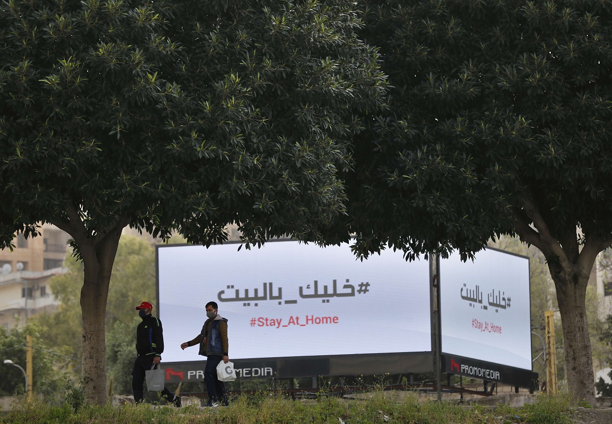 رجلان في بيروت يمران أمام لوحات اعلانية تعرض رسالة تحث المواطنين على البقاء في منازلهم 