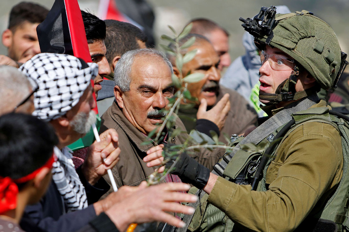Palestinian demonstrators confront an Israeli soldier during a protest against Israeli settlements