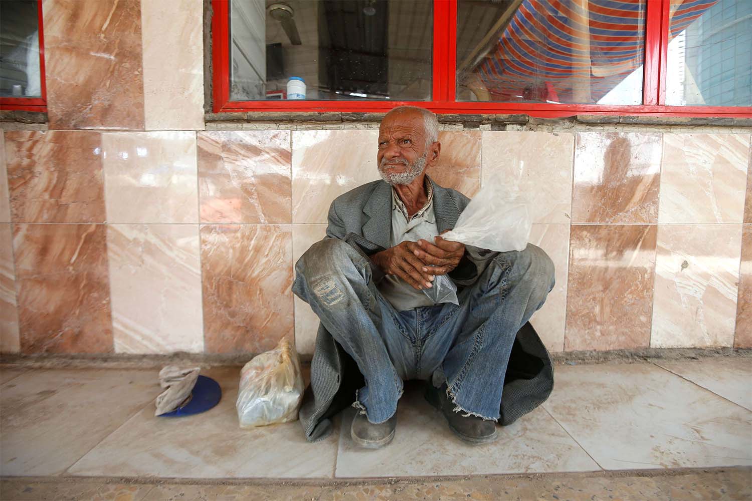 An Iraqi homeless man sits in front of a closed restaurant, during a curfew imposed to prevent the spread of coronavirus disease in Basra
