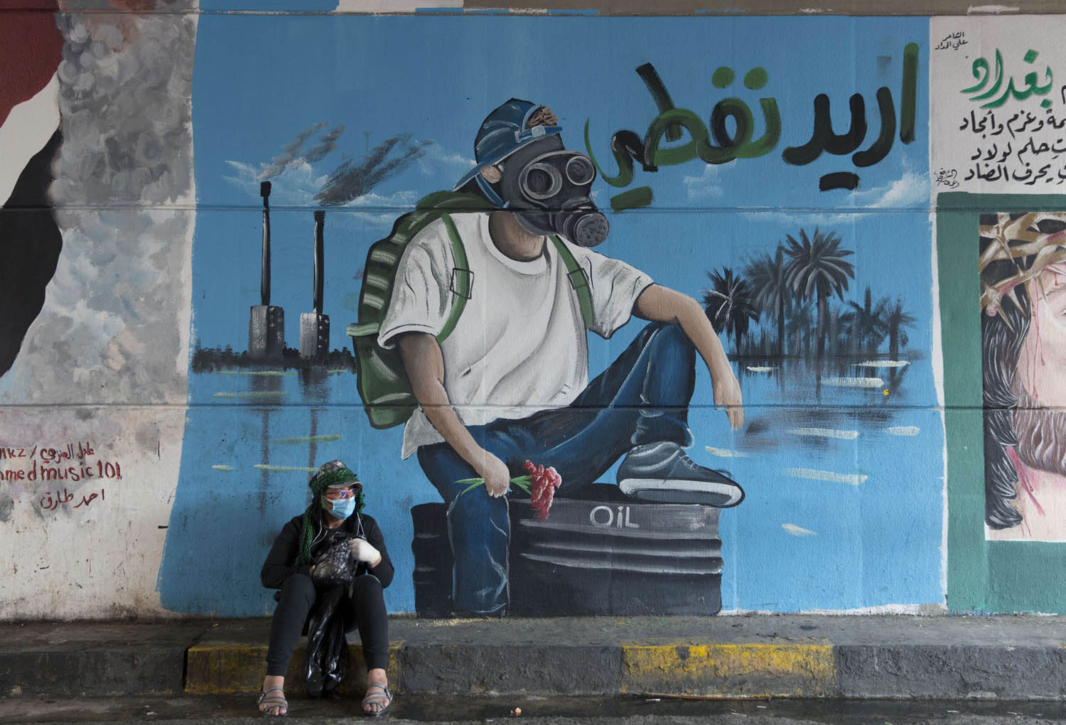 عراقي يرتدي كمامة يجلس امام ملصق في منطقة الاحتجاجات وسط بغداد