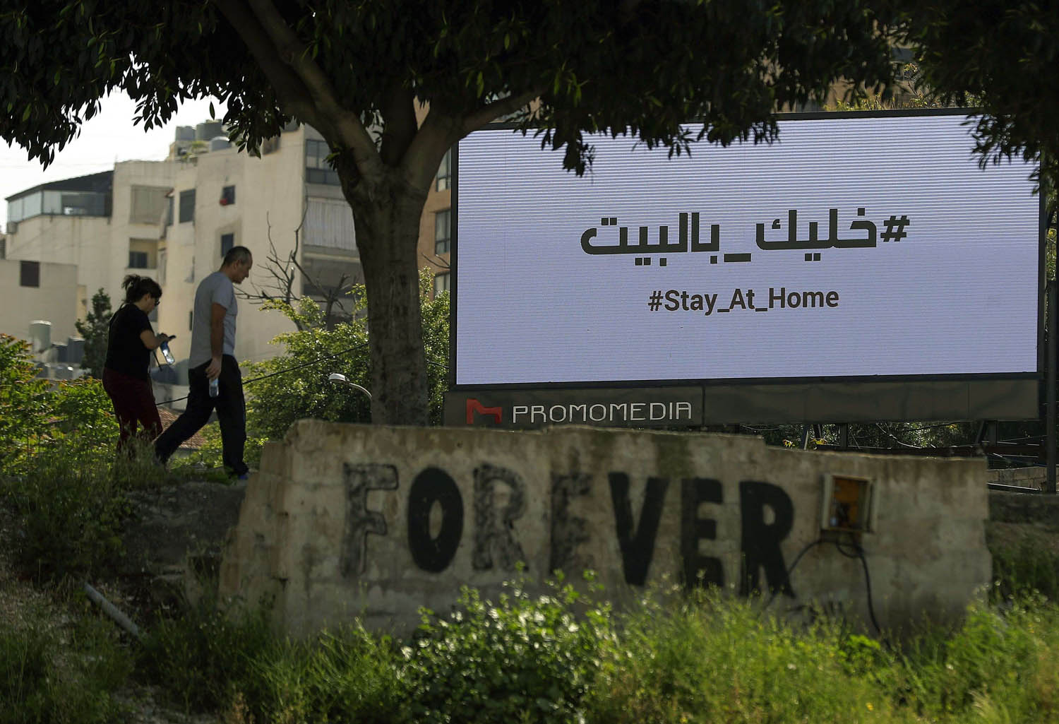لبنانيون يمرون بالقرب من شاشة تعرض اعلانا يحث على البقاء في المنازل