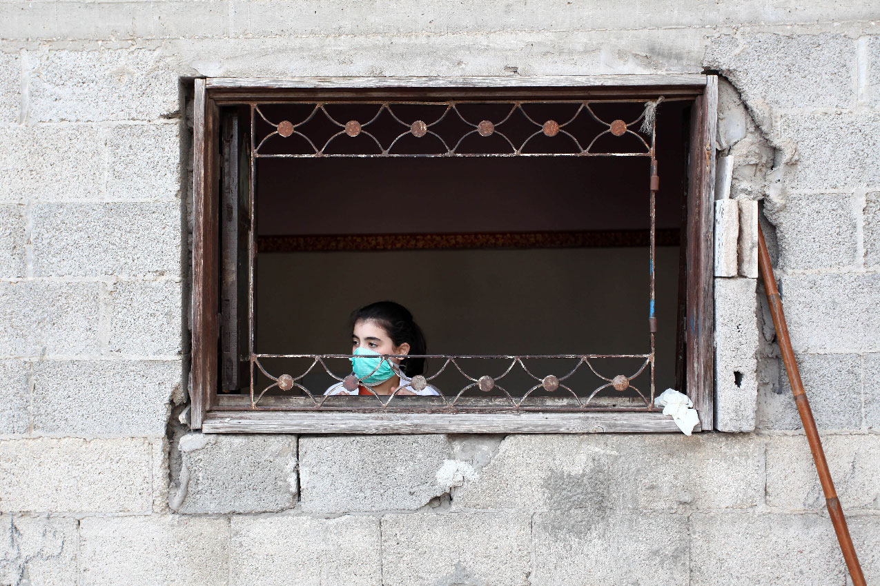 A girl wears a face mask as she looks out of the window in the Gaza Strip
