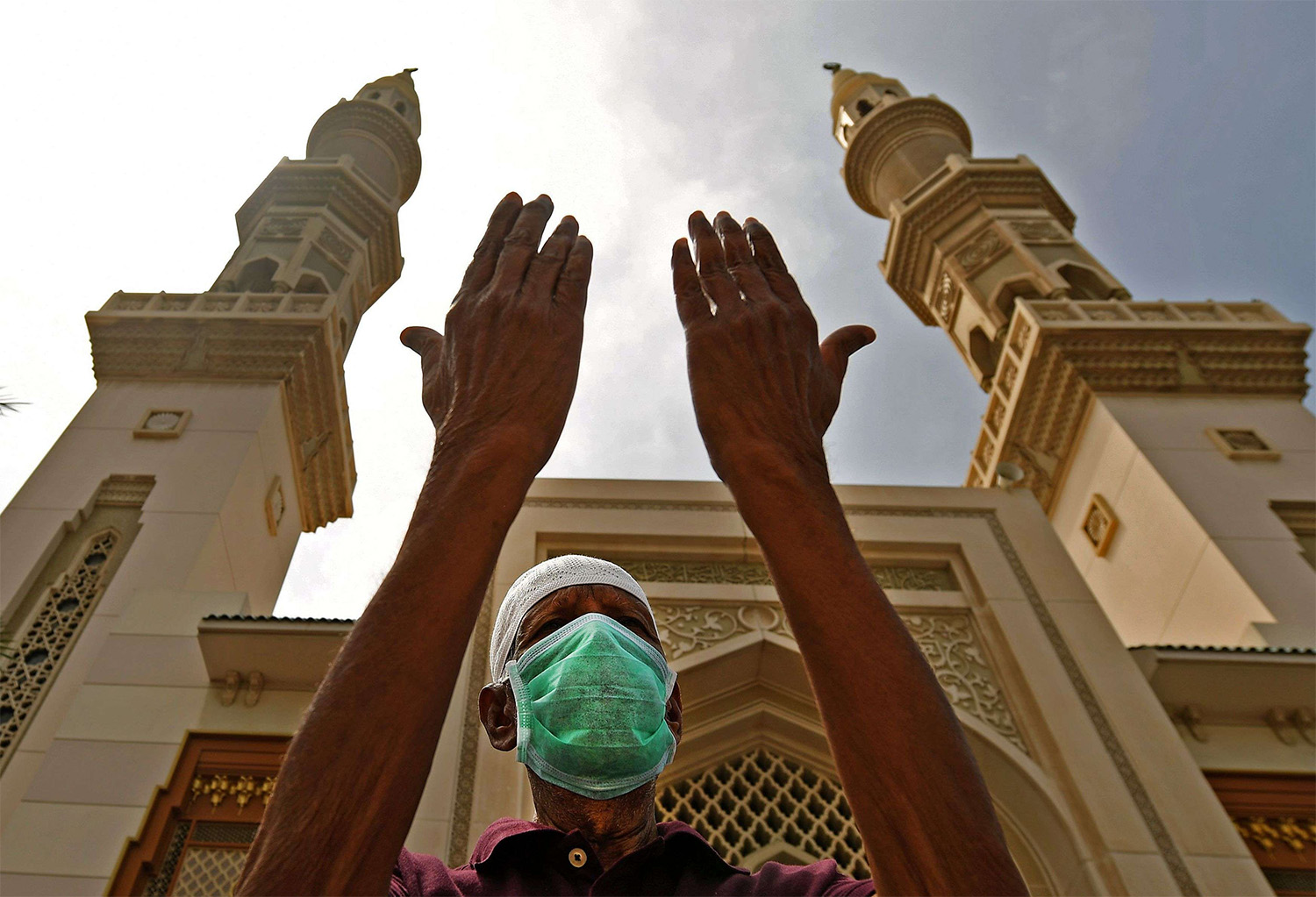 An elderly man wearing a protective mask lifts his hands in prayer outside a closed mosque in Sharjah 