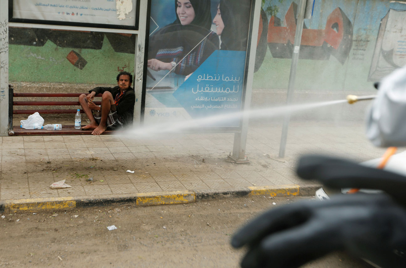 A man sits in an ad frame as health workers disinfect a street in Sanaa, Yemen