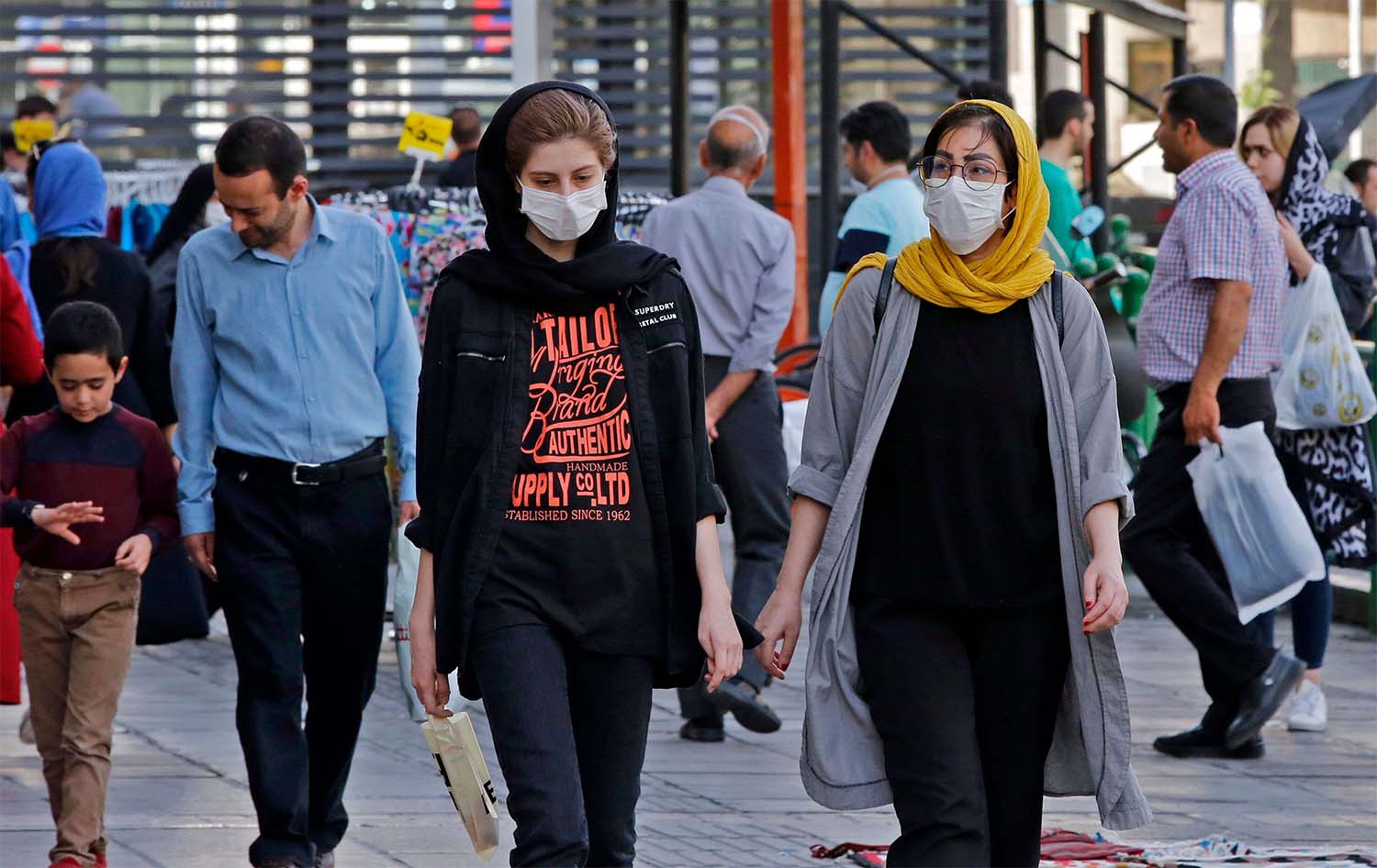 Iranians, some wearing face masks, walk along a street in the capital Tehran