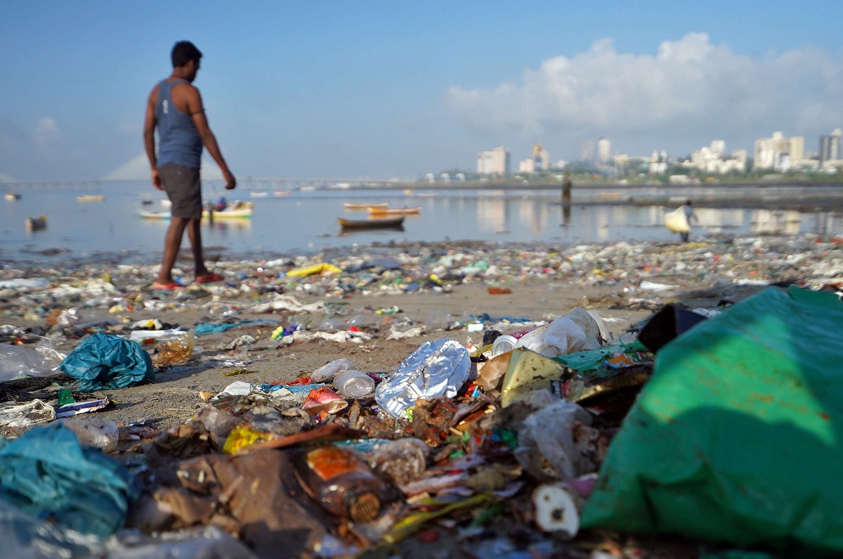 رجل يمشي على شاطئ مليء بالمخلفات البلاستيكية في مومباي بالهند