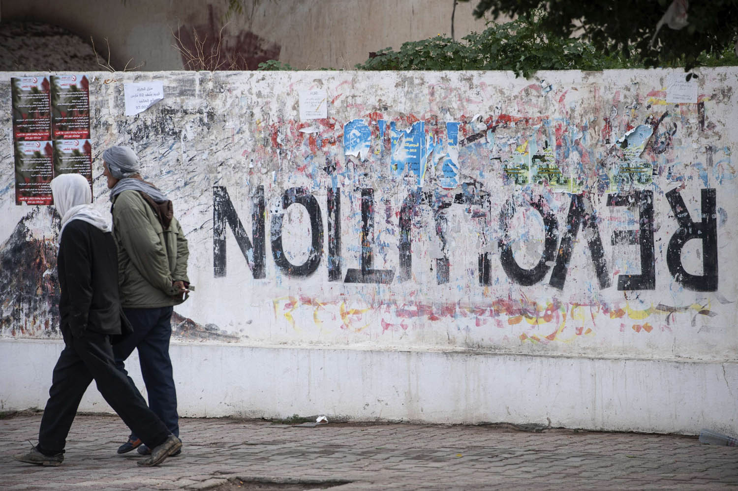 تونسيون يمرون بجانب غرافيتي للثورة مكتوب بالمقلوب