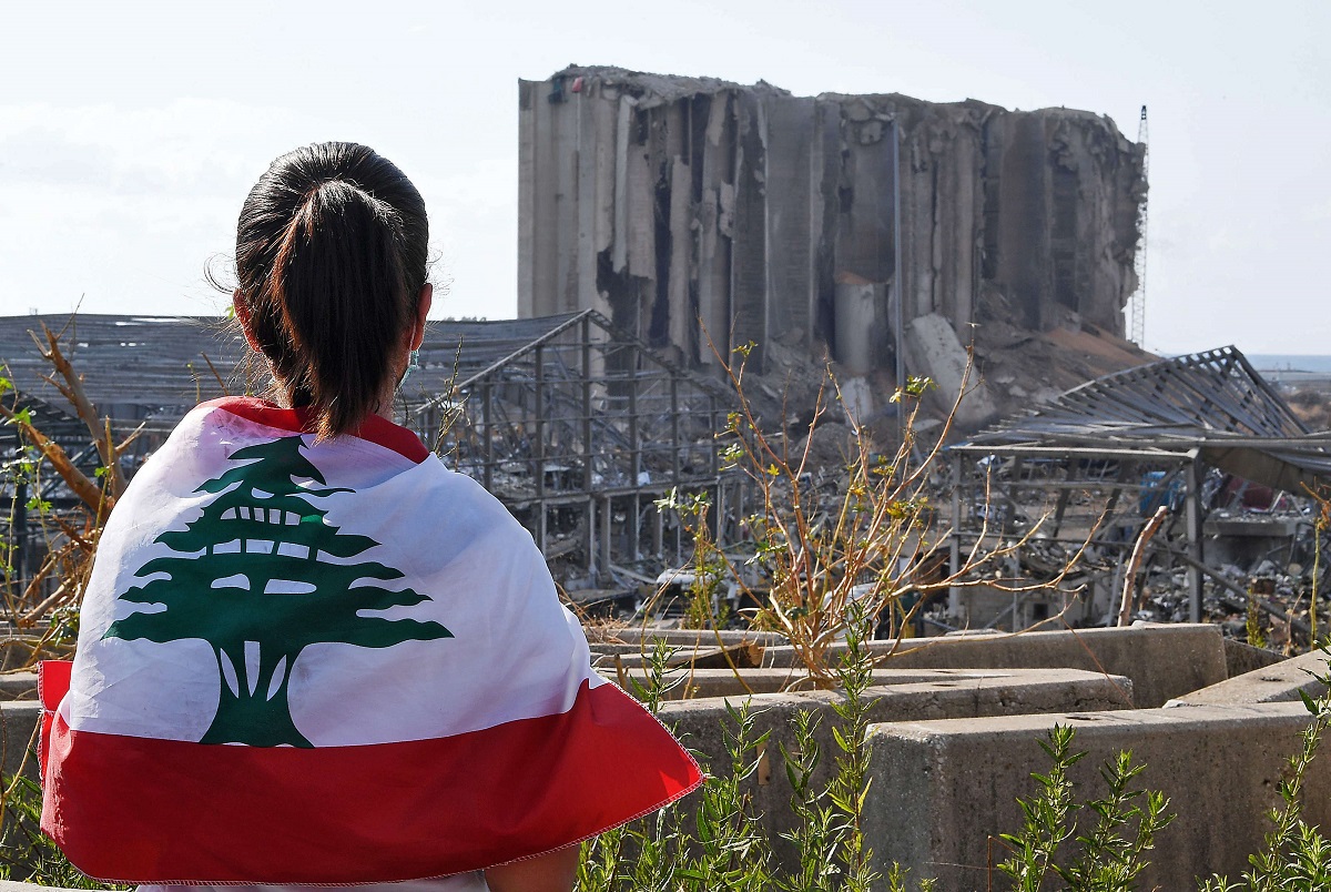 فتاة لبنانية ترتدي علم بلادها وتطل على مرفأ بيروت المدمر