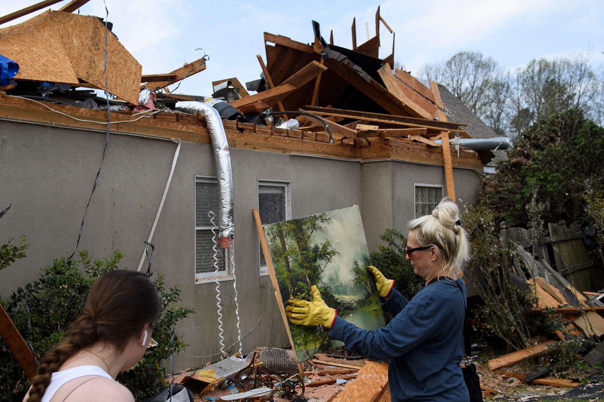 سيدة تلتقط لوحة من حطام منزلها المدمر في مارس 2021 بعد إعصار ضرب ألاباما الأميركية