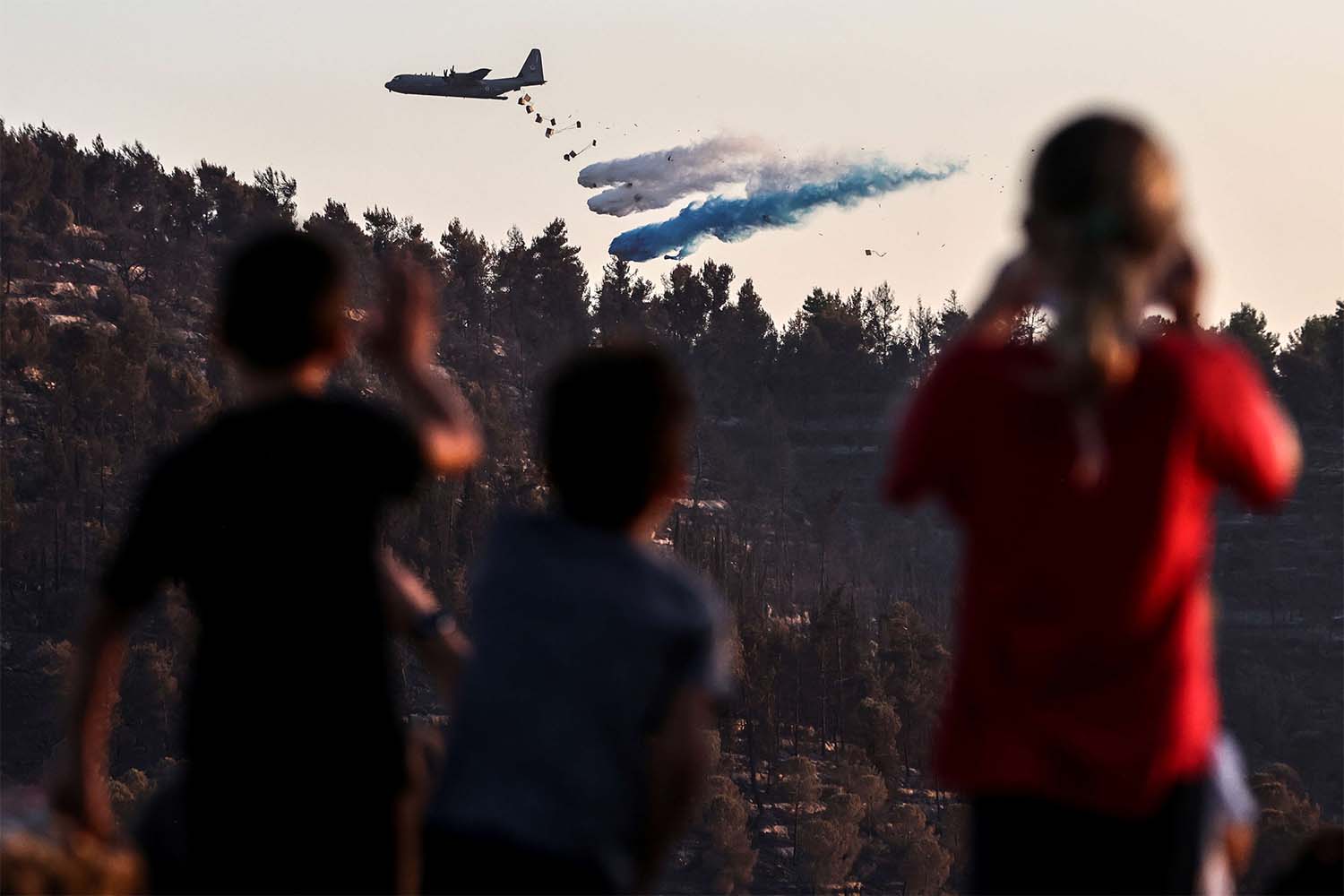 Children look on as an Israeli military plane disperses fire retardant to extinguish a fire near the Israeli kibbutz of Tzuba