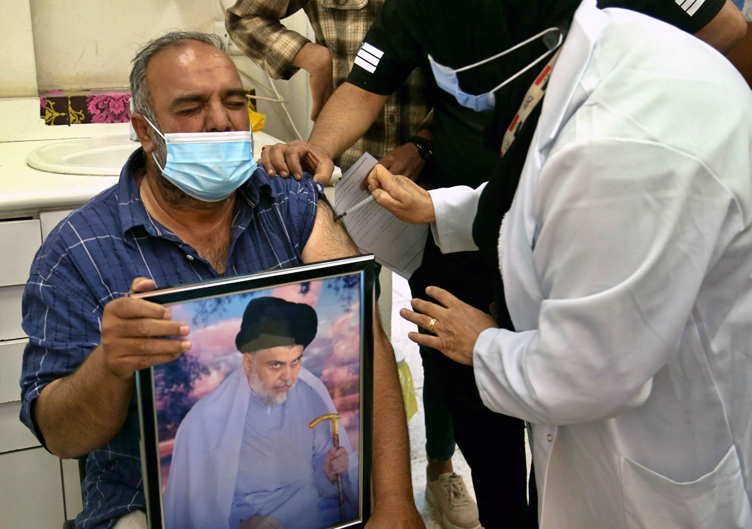 عراقي يحمل صورة مقتدى الصدر يتلقى لقاحا مضادا لكورونا
