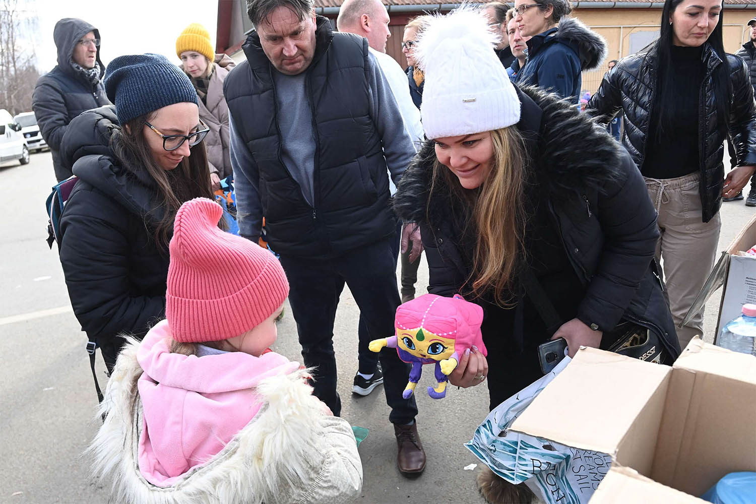 A woman offers a toy to a girl after Ukrainian refugees crossed the Ukrainian-Hungarian border in Tiszabecs
