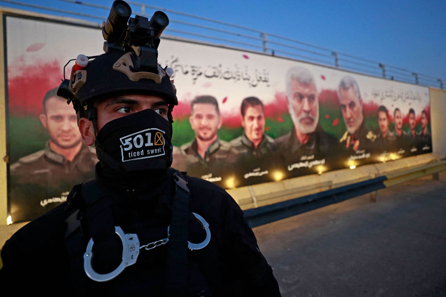 مقاتل في الحشد الشعبي أمام جدارية تمجد سليماني والمهندس