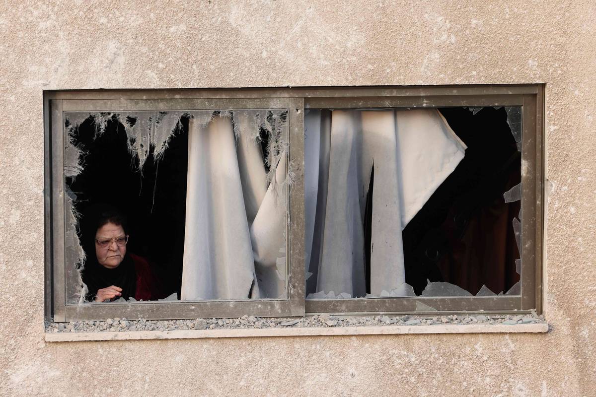 فلسطينية تنظر من زجاج بيتها المحطم على آثار القصف الإسرائيلي في غزة