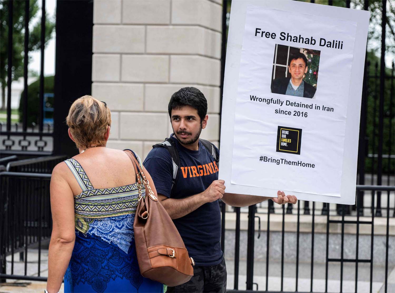 Darian Dalili speaks with a woman as he holds up a sign during a hunger strike outside the White House in Washington, DC on August 14, 2023