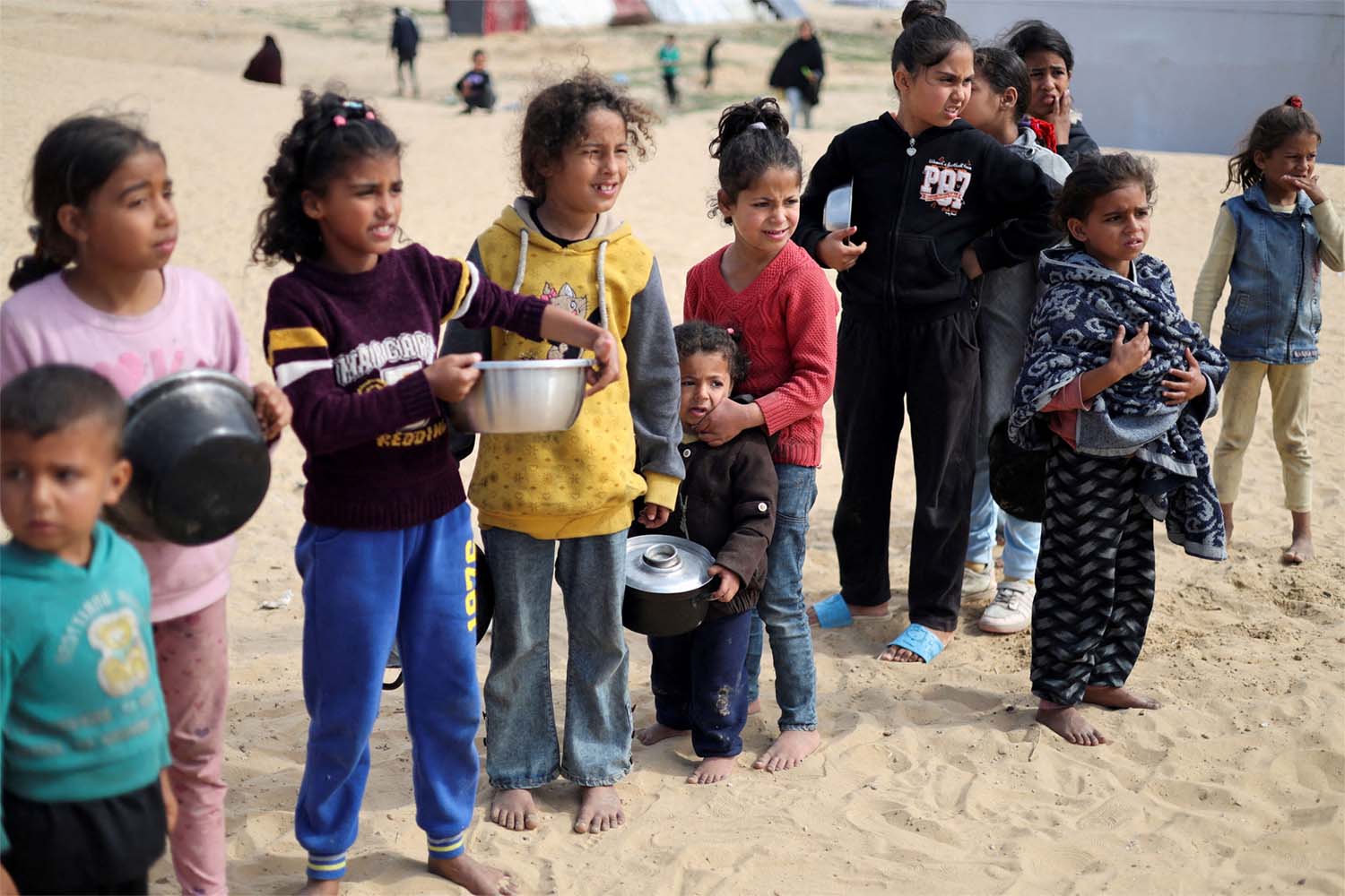 Displaced Palestinian children wait to receive free food at a tent camp amid food shortages