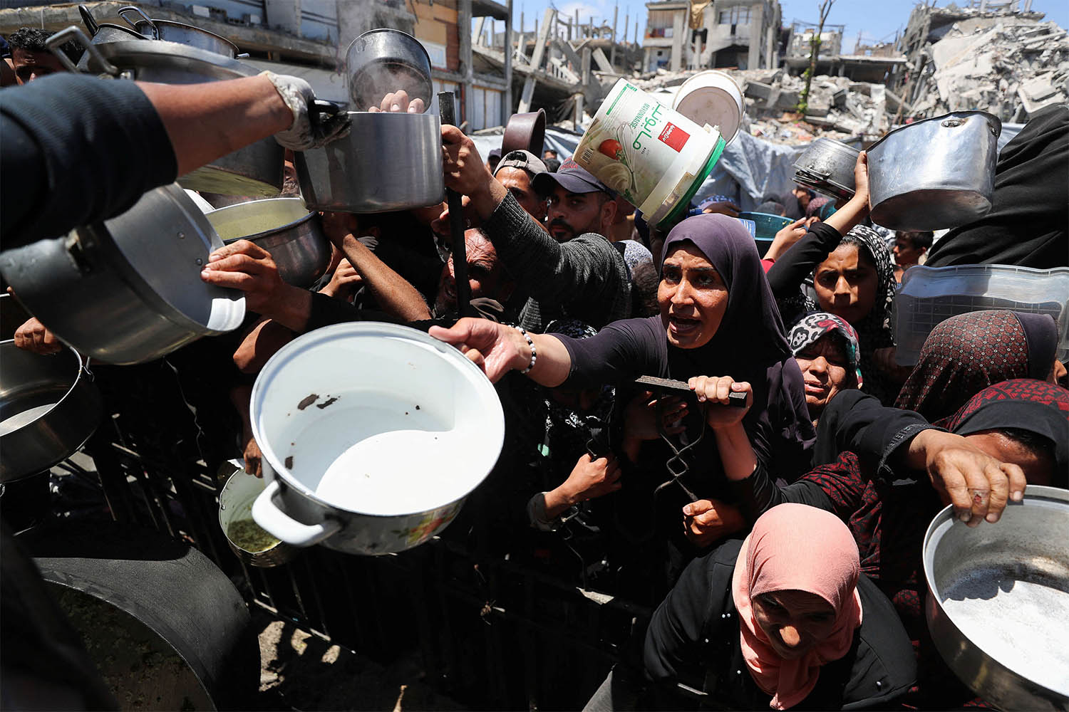Palestinians wait to receive food cooked by a charity kitchen, in Beit Lahia