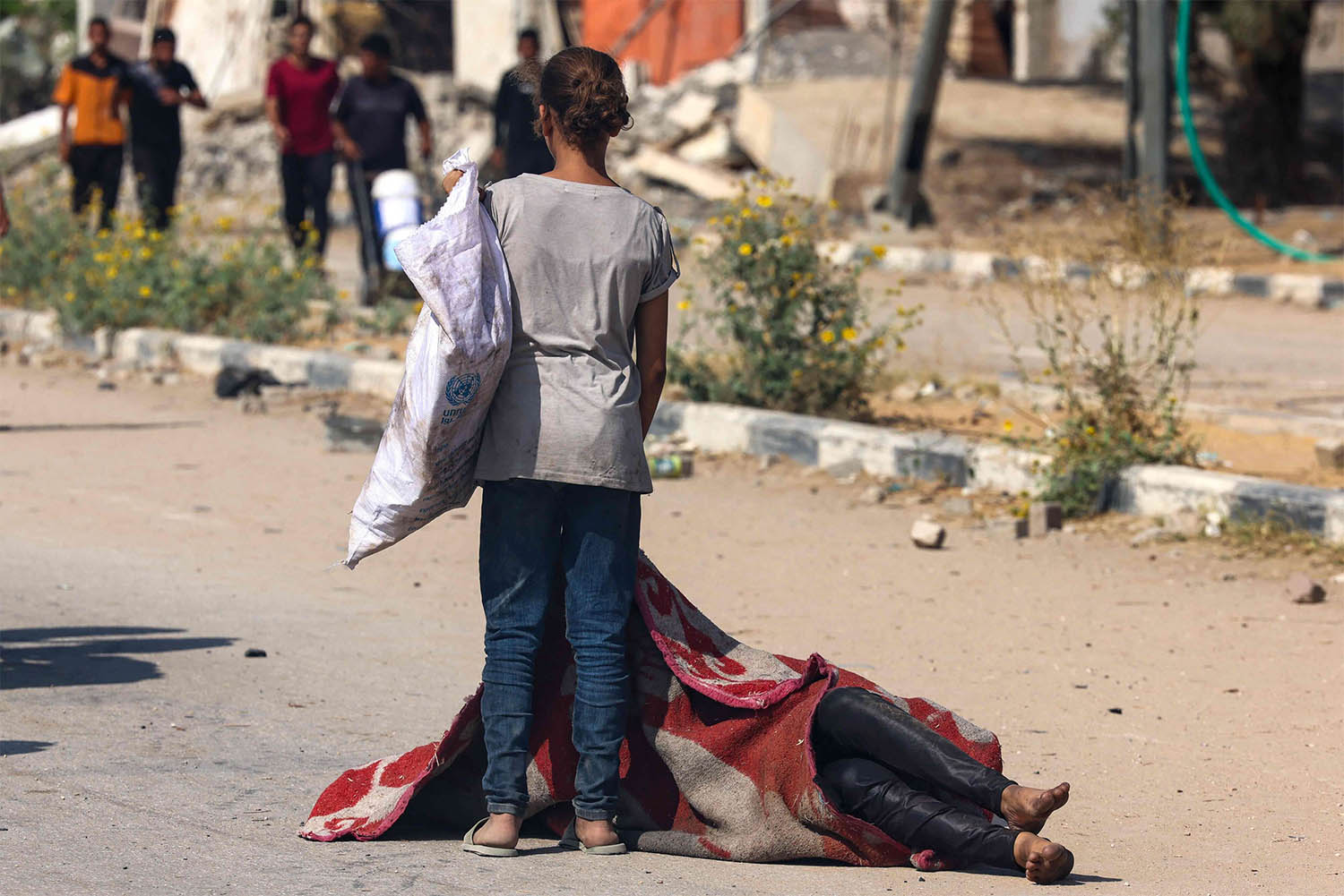 A Palestinian girl stands over the covered body of a person who was killed while seeking food at a distribution point run by the US and Israeli-backed Gaza Humanitarian Foundation group, in Nusseirat