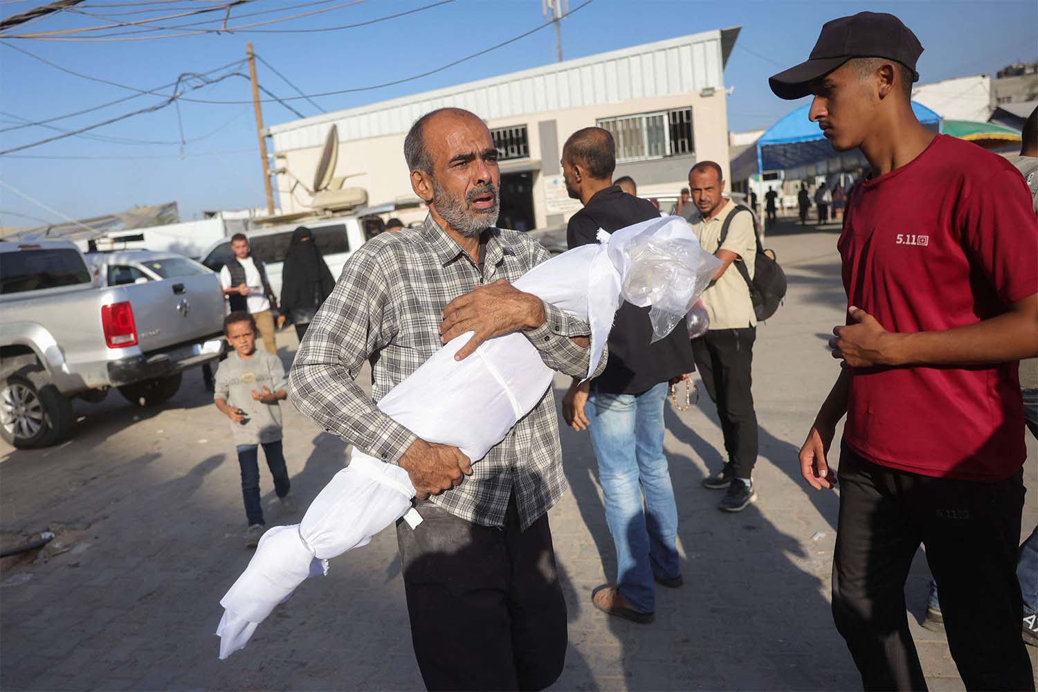 A Palestinian man carries the draped body of a child killed in Israeli strikes the previous day on the central Gaza Strip, outside the Shuhada al-Aqsa hospital