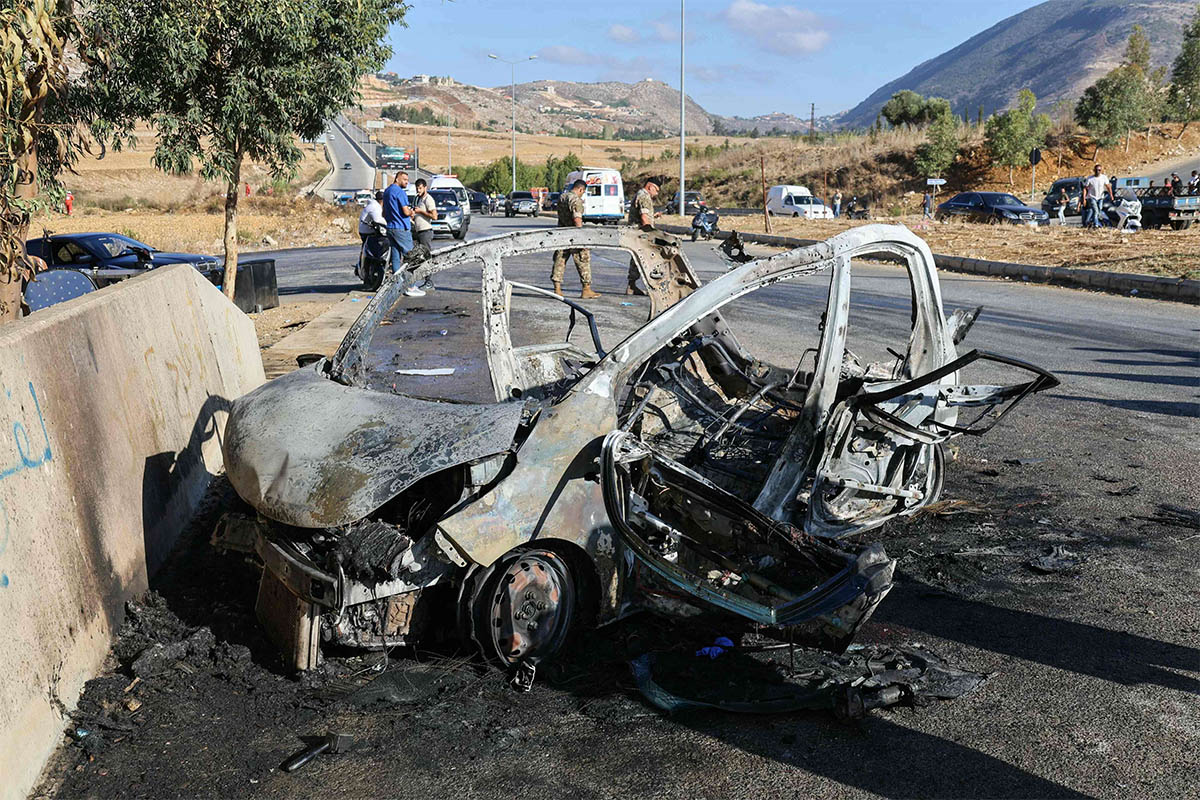Lebanese emergency and security service members deploy around the wreckage of a car hit by an Israeli drone attack in the southern area of Al-Jarmak 