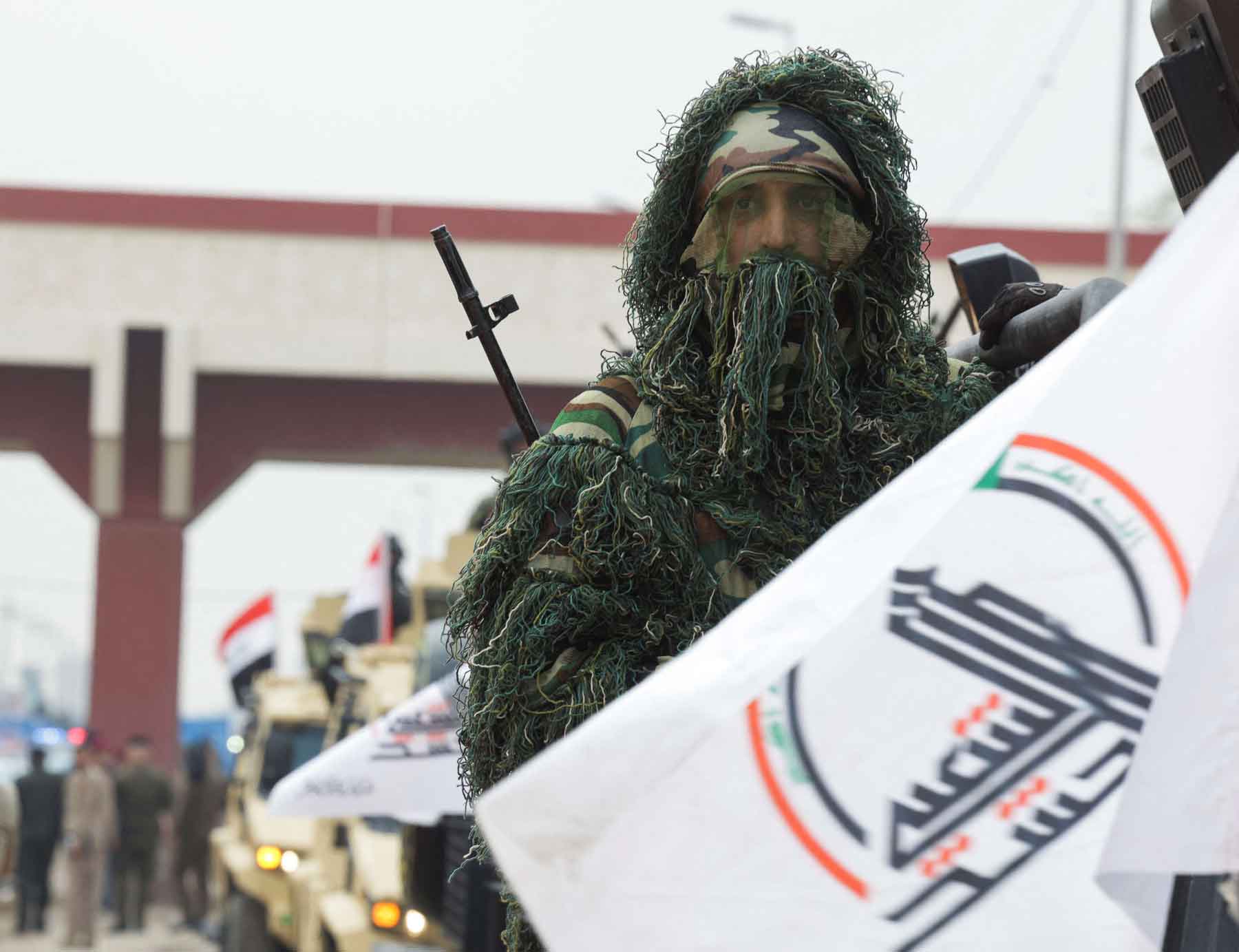 A member of Iraq’s Popular Mobilisation Forces (PMF) rides in a military vehicle next to a flag during a parade in Baghdad, December 10, 2025. 