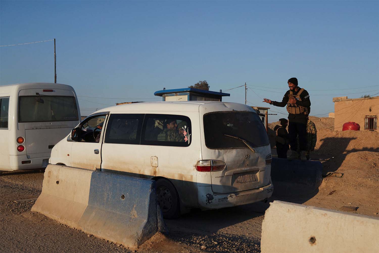 A member of the Syrian army interacts with other members of the Syrian army siting in a vehicle, which is headed to Al-Hasakah