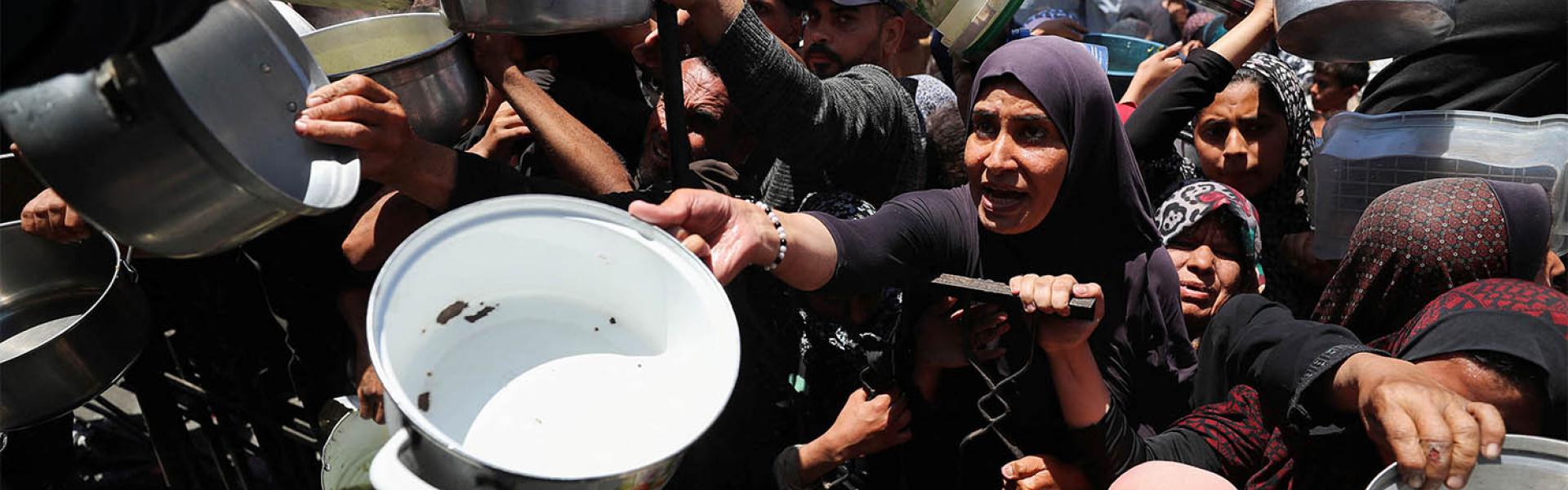 Palestinians wait to receive food cooked by a charity kitchen, in Beit Lahia