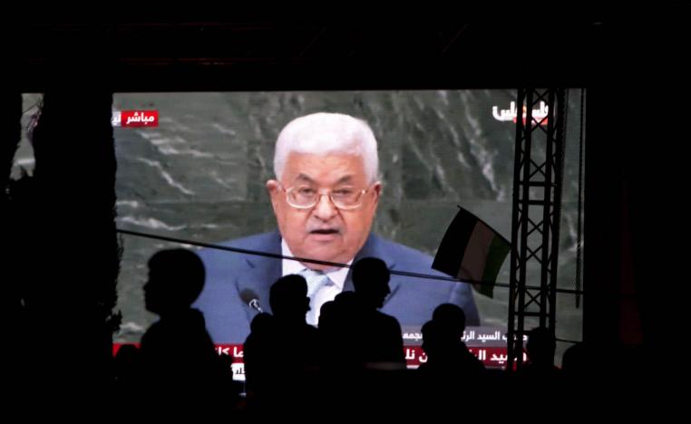 فلسطينيون يتحدثون على خلفية شاشة تنقل خطاب الرئيس الفلسطيني عباس في الأمم المتحدة