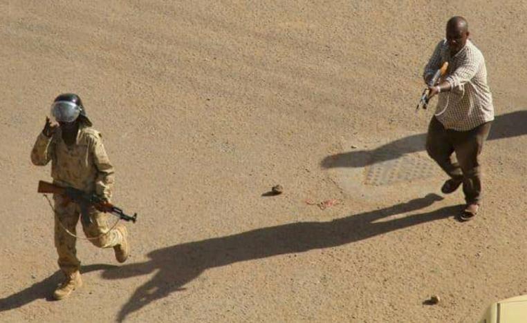 In this Dec. 25, 2018 file image, provided by a Sudanese activist, a plain clothed policeman points his rifle at protesters during clashes in Khartoum, Sudan.