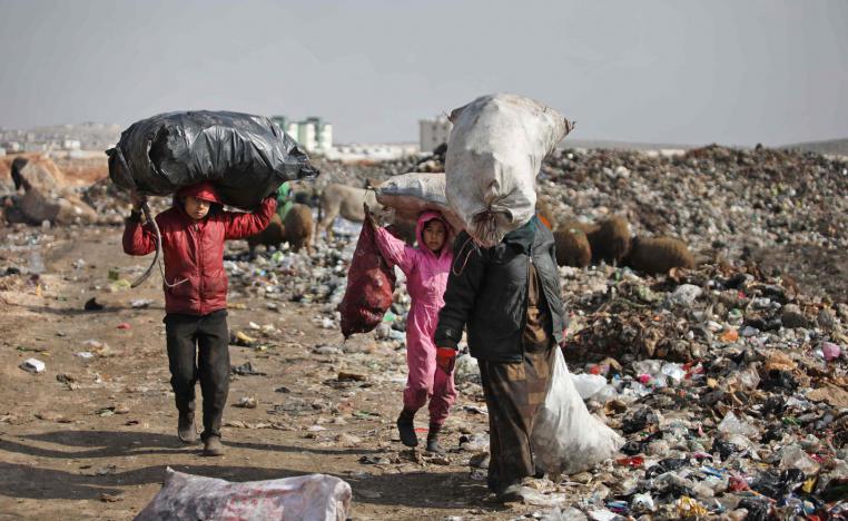 A displaced Syrian woman and children carry over their heads bags of collected trash at a landfill outside a camp in Kafr Lusin near the border with Turkey in Idlib province in northwestern Syria, on January 29, 2019.