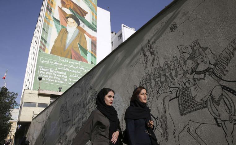 Iranian women walk past a portrait of the late revolutionary founder Ayatollah Khomeini and paintings of Persian poetry in Tehran, Iran, Monday, May 7, 2018.