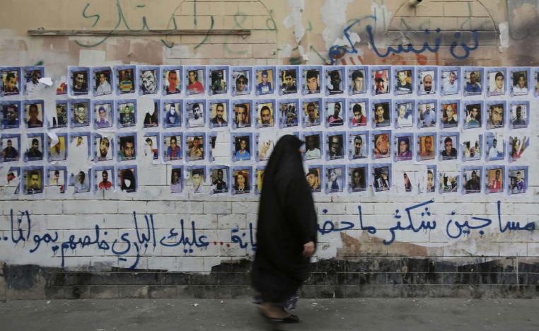 A Bahraini woman walks past images of political prisoners plastered on a wall in Sanabis, Bahrain