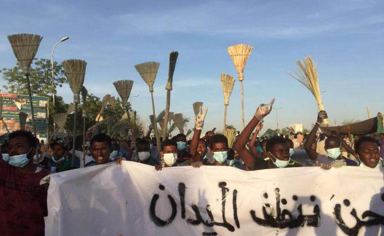 سودانيون يتظاهرون رافعين المكانس أمام مبنى قيادة الجيش
