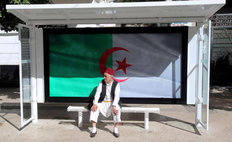 A man sits at a bus station decorated with the national flag during a protest demanding the removal of Algeria’s ruling elite in Algiers
