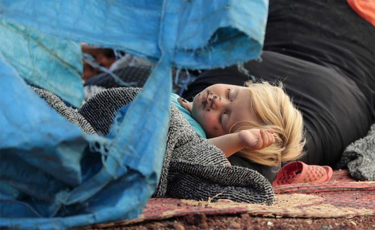 A displaced Syrian child sleeps on a mat laid out on the floor in an olive grove in the town of Atmeh, Syria