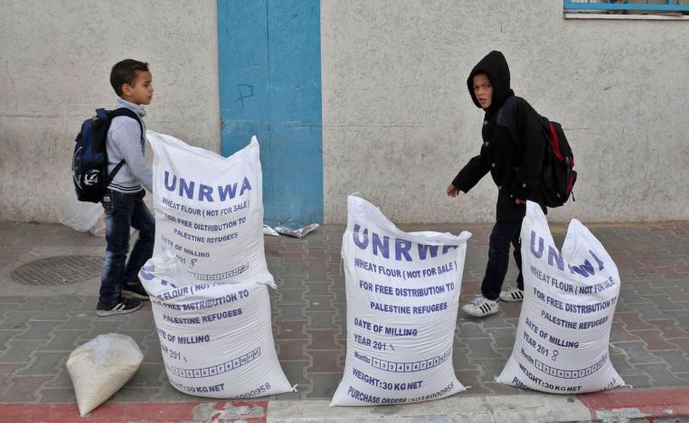 أطفال فلسطينيون يمرون بالقرب من أكياس لوكالة الغوث الدولية في مخيم للاجئين في رفح