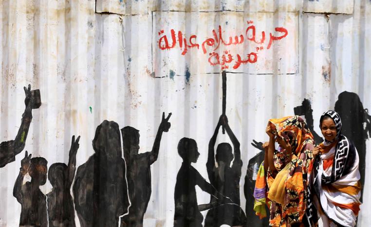 سودانيات بالقرب من جدارية عن شعارات الثورة