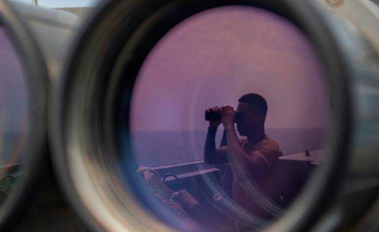 A US sailor uses binoculars to scan the ocean during a bridge watch aboard a US guided-missile destroyer in the Gulf