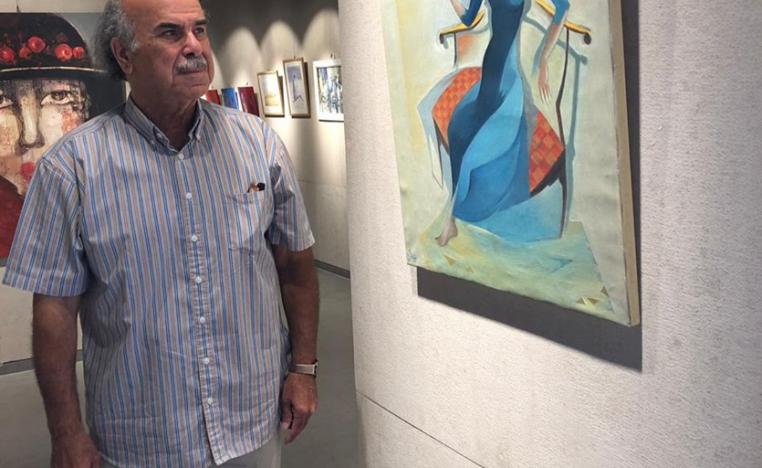 الفنان عبدالهادي شلا يقف أمام لوحة من لوحات المعرض (الصورة من صفحة الفنان على فيسبوك)