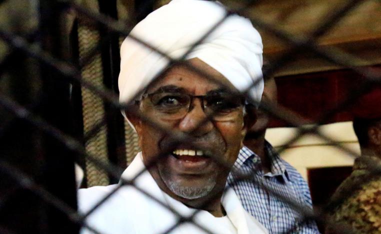 Sudan's former president Omar Hassan al-Bashir smiles as he is seen inside a cage at the courthouse where he is facing corruption charges
